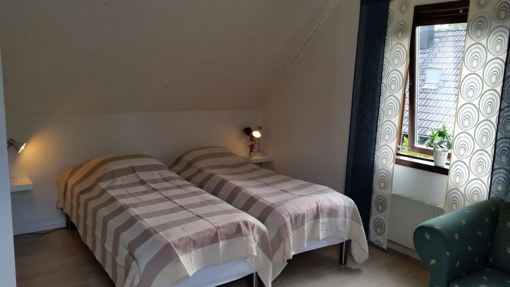 Bedroom with two beds side by side, reading lamps and an armchair by the window